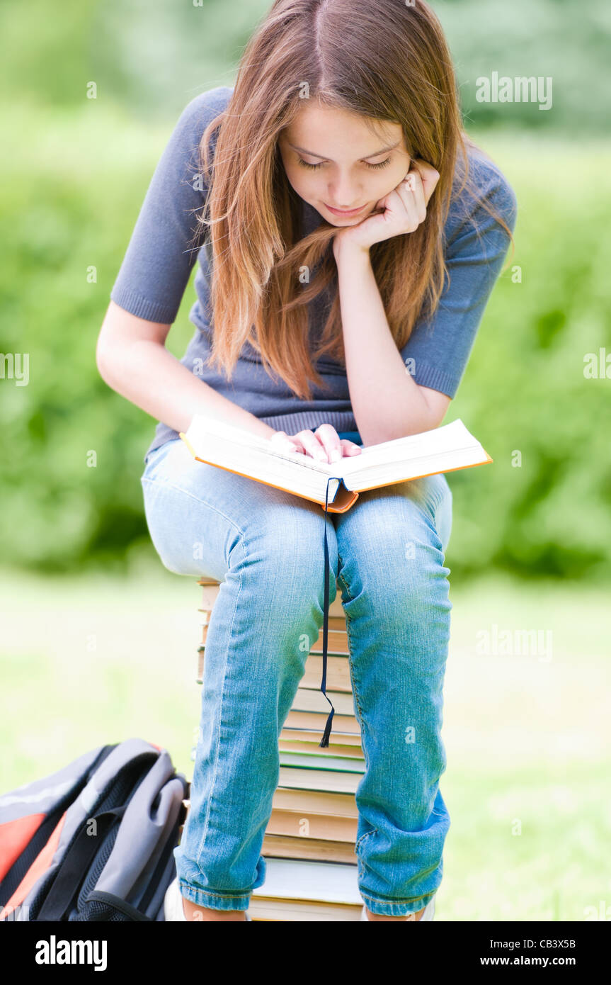 beautiful and happy young student girl sitting on pile of books ...