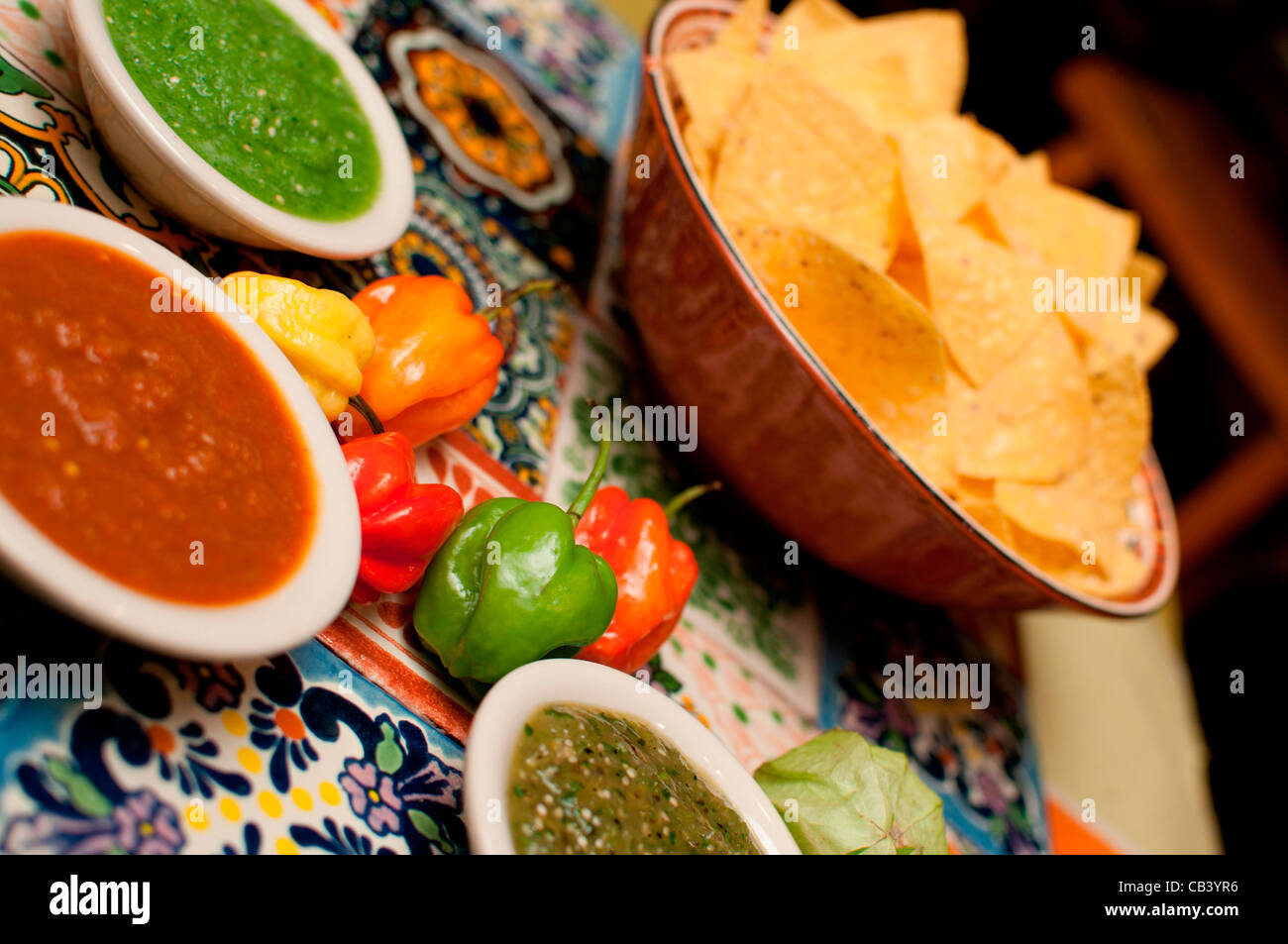 Close up of tortilla chips, peppers and salsa on colored tiles Stock Photo