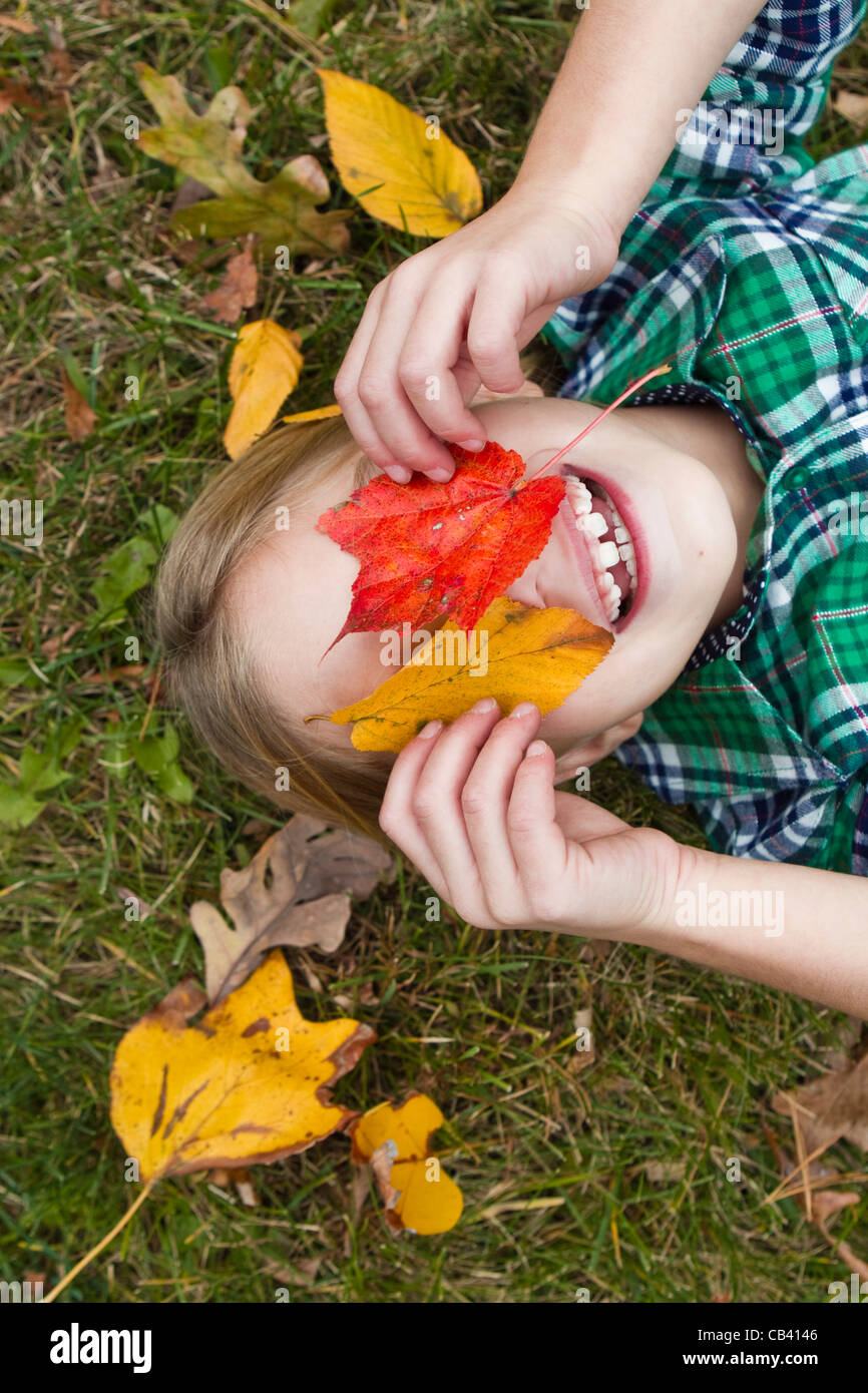Smiling girl holding Autumn leaves in front of face, lying on grass ...