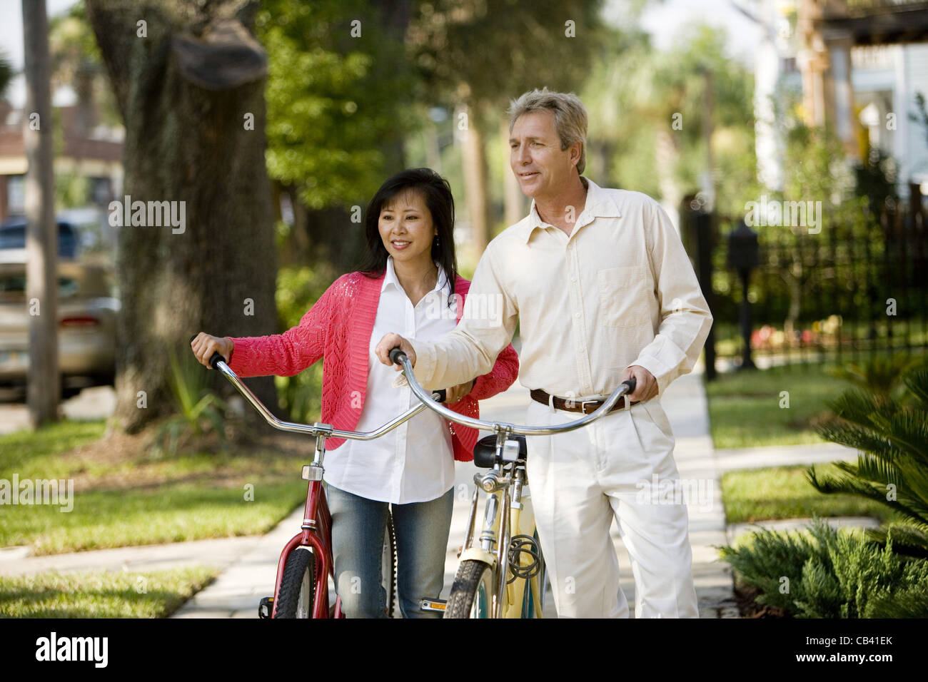 A mature inter-racial couple walking with bicycles in their neighborhood Stock Photo