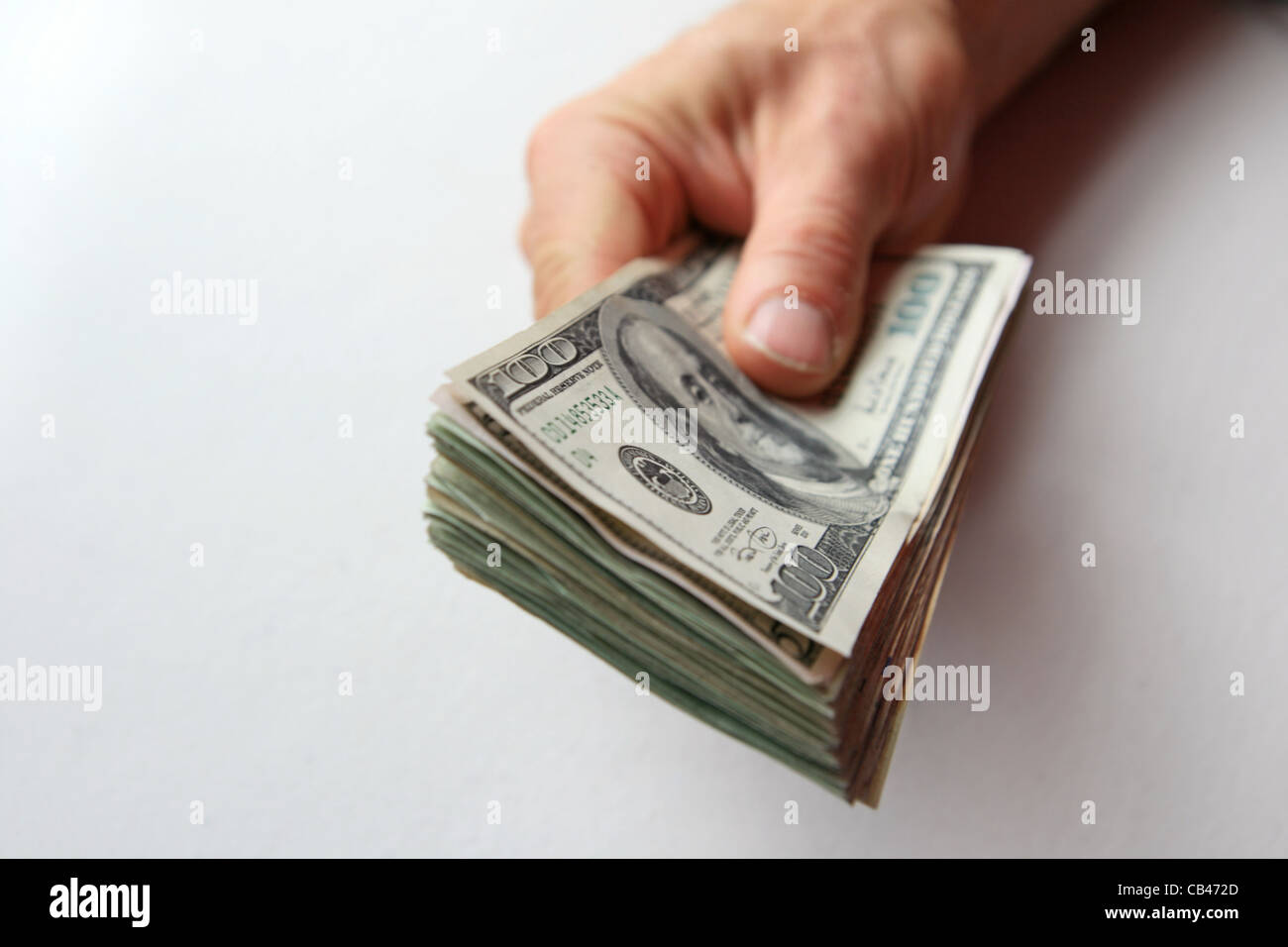 a man's hand holds a stack of US money with 100 dollar bill on top and shallow depth of field Stock Photo