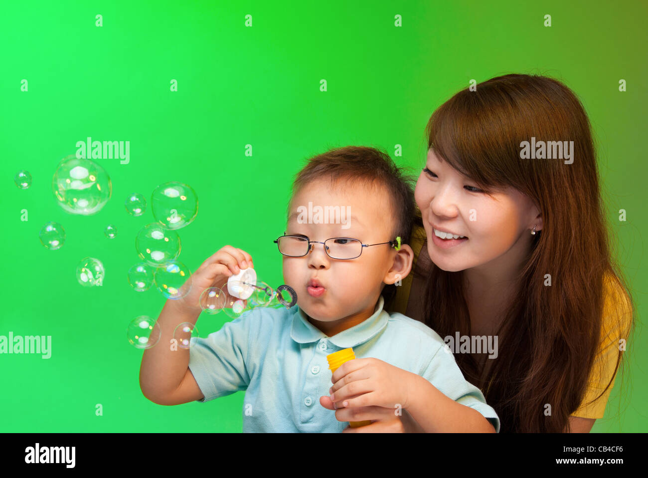 Mother and son blowing soap bubbles with Chinese appearance on green background Stock Photo