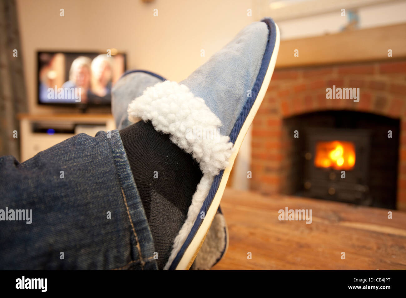 feet up watching the television with log burning stove in the background Stock Photo