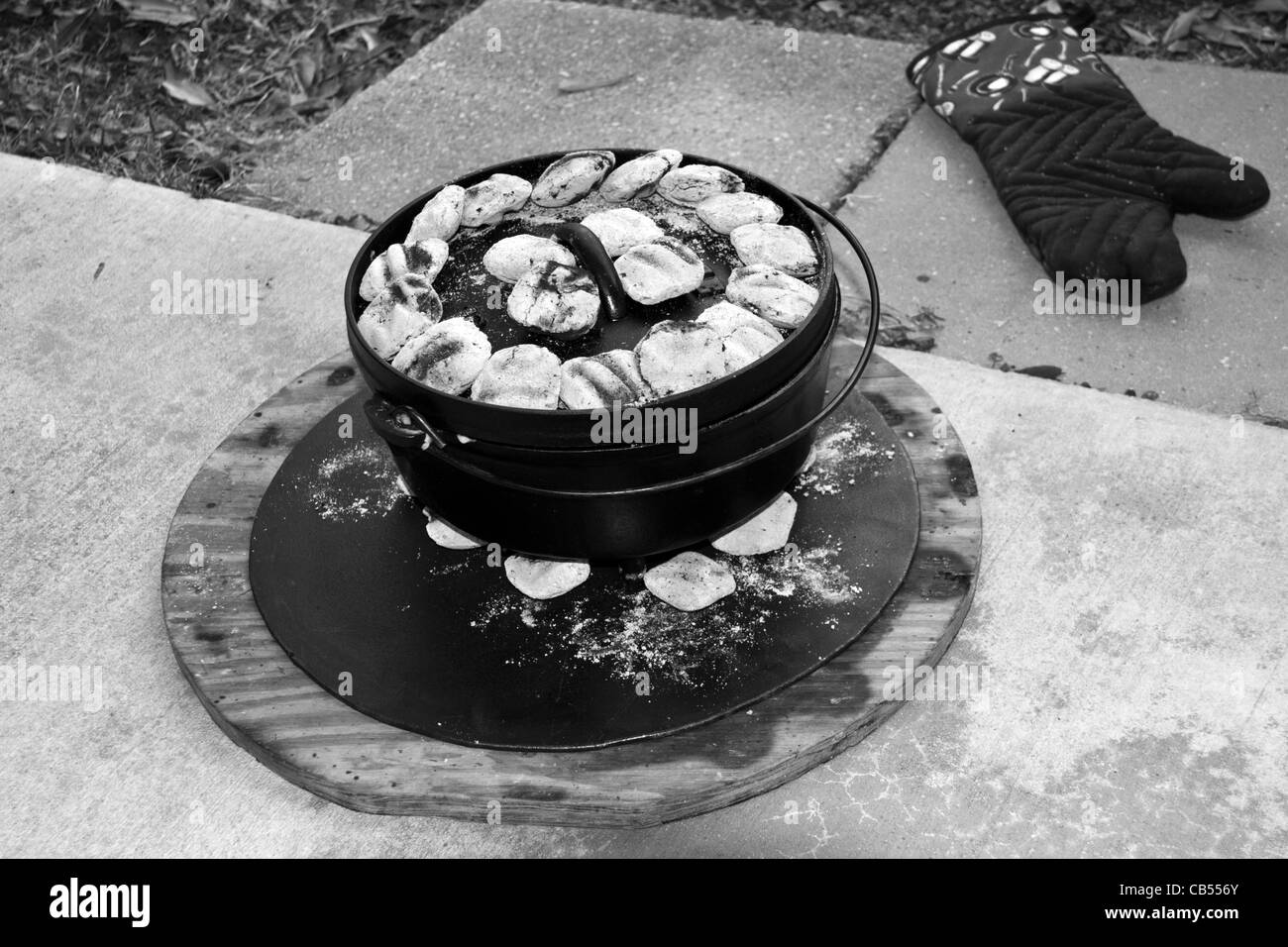 Dutch Oven outdoor cooking using cast iron pots with metal base support and heavy duty cooking mitt. Stock Photo