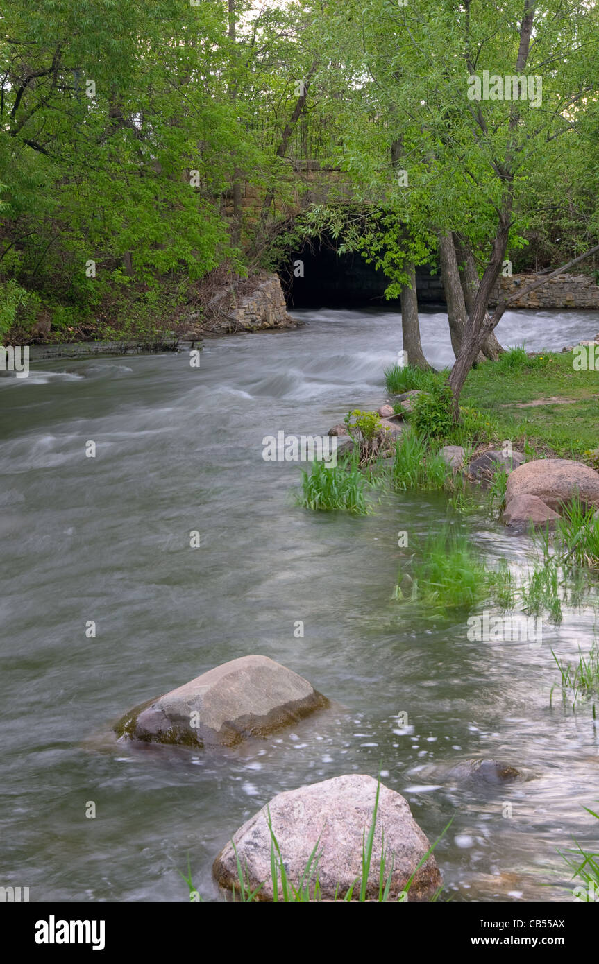 waters of minnehaha creek in minnehaha park overflowing their banks and running under viaduct Stock Photo