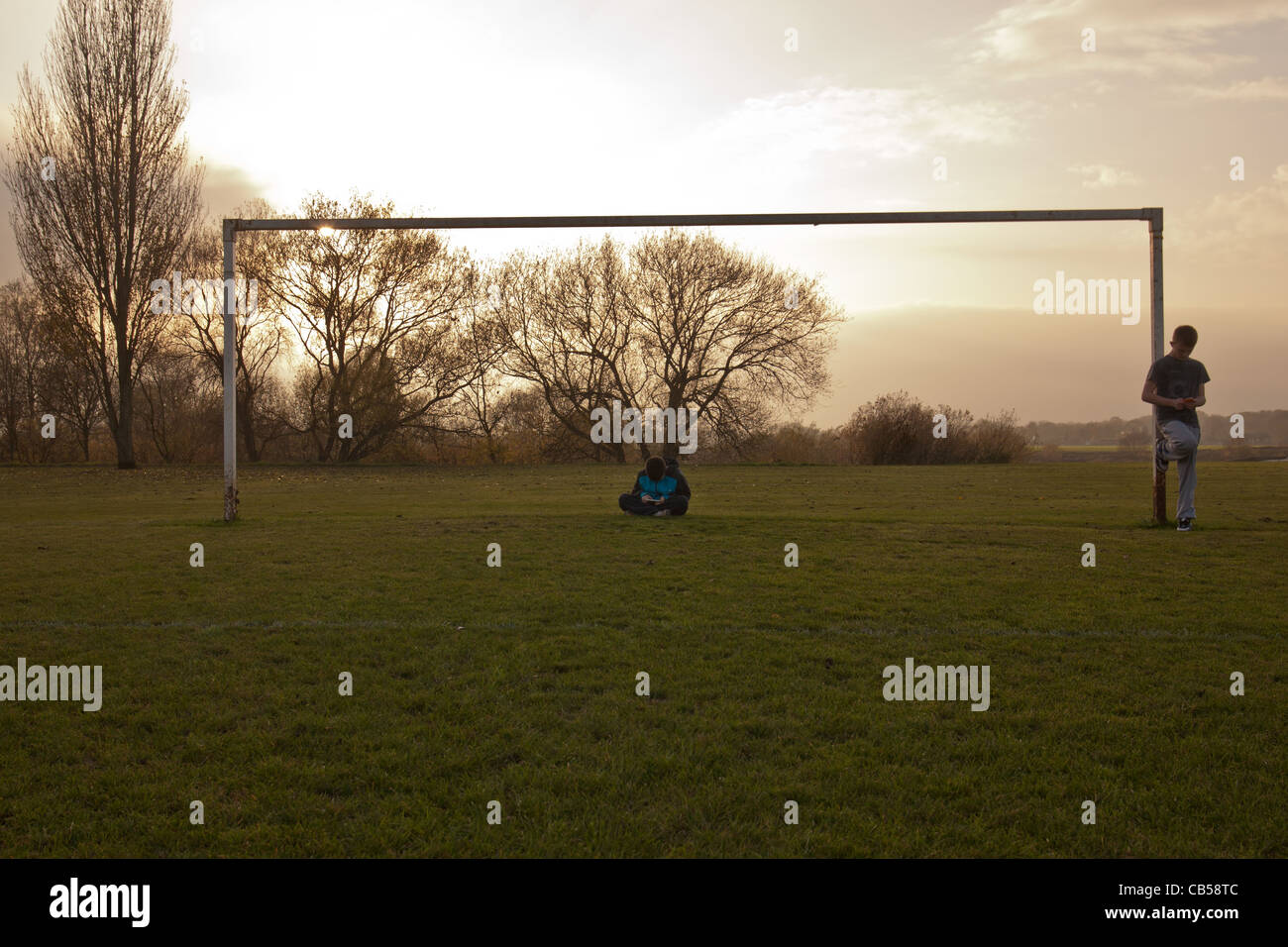 Kids of today. Two children playing on their phones in an empty goal post. Stock Photo