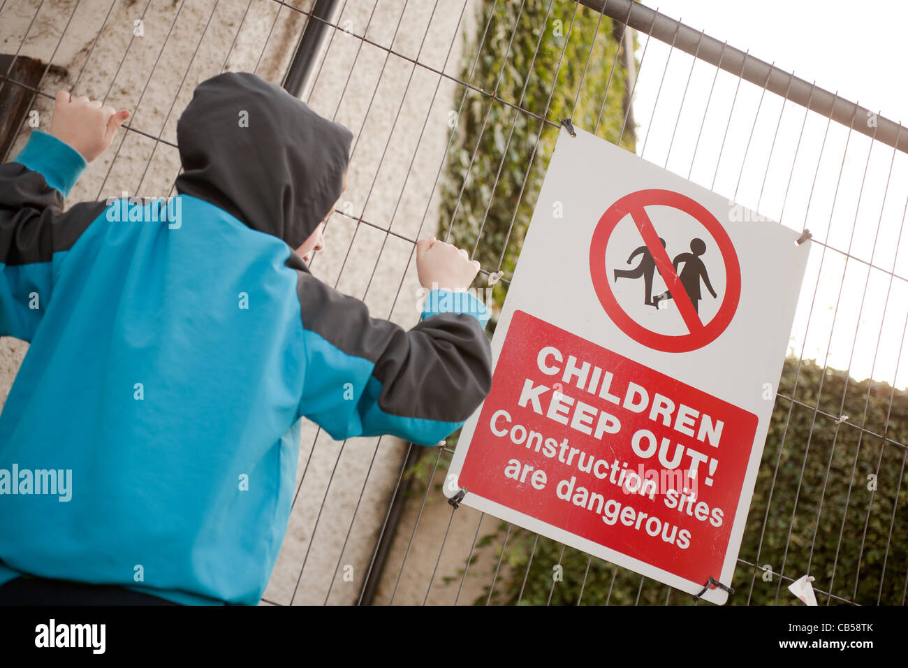 A young boy climbing a fence with warning signs Stock Photo