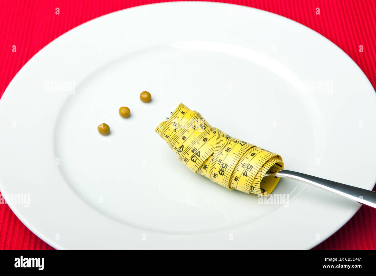 Plate with three peas and a measuring tape around a fork. Stock Photo