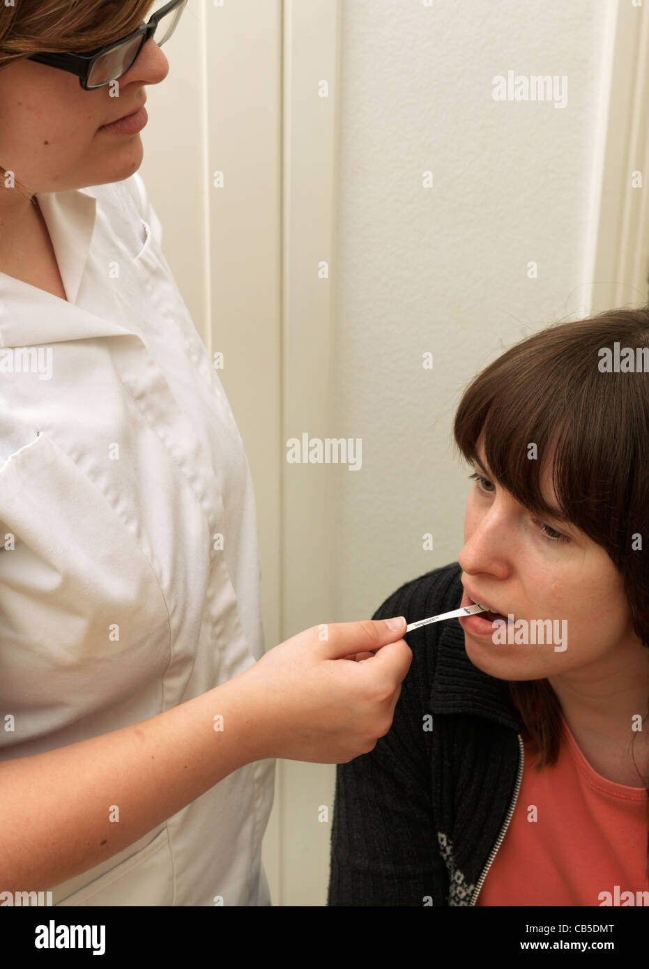 A Nurse Placing An Oral Paper Thermometer (Tempa DOT) In A Patient's Mouth Taking Her Temperature Stock Photo
