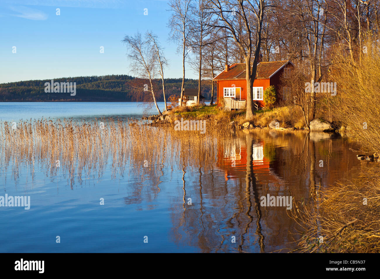 Typical Swedish or Scandinavian red wooden house by a lake. Lake Sävelången, Ingared, Västra Götaland, Sweden  Model Release: No.  Property Release: No.  Info: Photographer's understanding (but not guaranteed) is that property release is not needed for private properties for commercial use according to swedish law for images taken from public land/road. Image taken from public road. Stock Photo