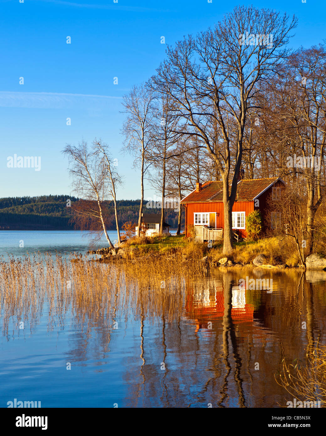 Typical Swedish or Scandinavian red wooden house by a lake. Lake Sävelången, Ingared, Västra Götaland, Sweden  Model Release: No.  Property Release: No.  Info: Photographer's understanding (but not guaranteed) is that property release is not needed for private properties for commercial use according to swedish law for images taken from public land/road. Image taken from public road. Stock Photo