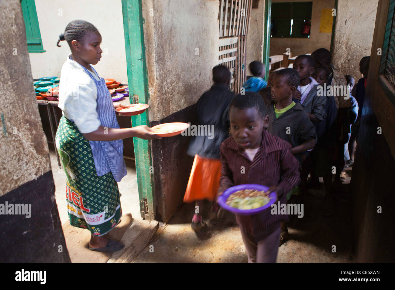 School children receive freshly cooked food at Kibera School, Nairobi where an NGO runs a lunchtime feeding program. Stock Photo