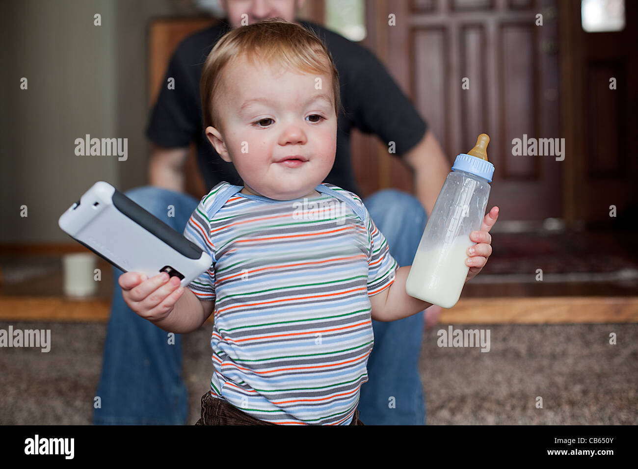 Toddler boy holding has bottle and a smart phone in his hands. Stock Photo