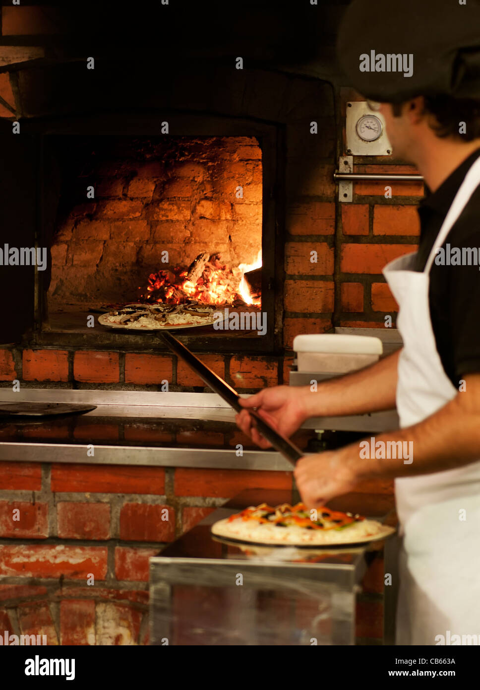 A chef putting a pizza in a wood-fired oven in the classic Italian style Stock Photo