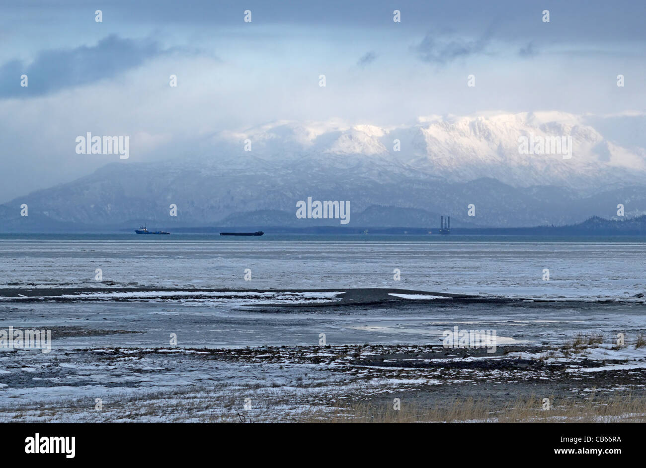Kenai mountains rising above Mud Bay in winter with barges and a drilling rig in the background. Stock Photo