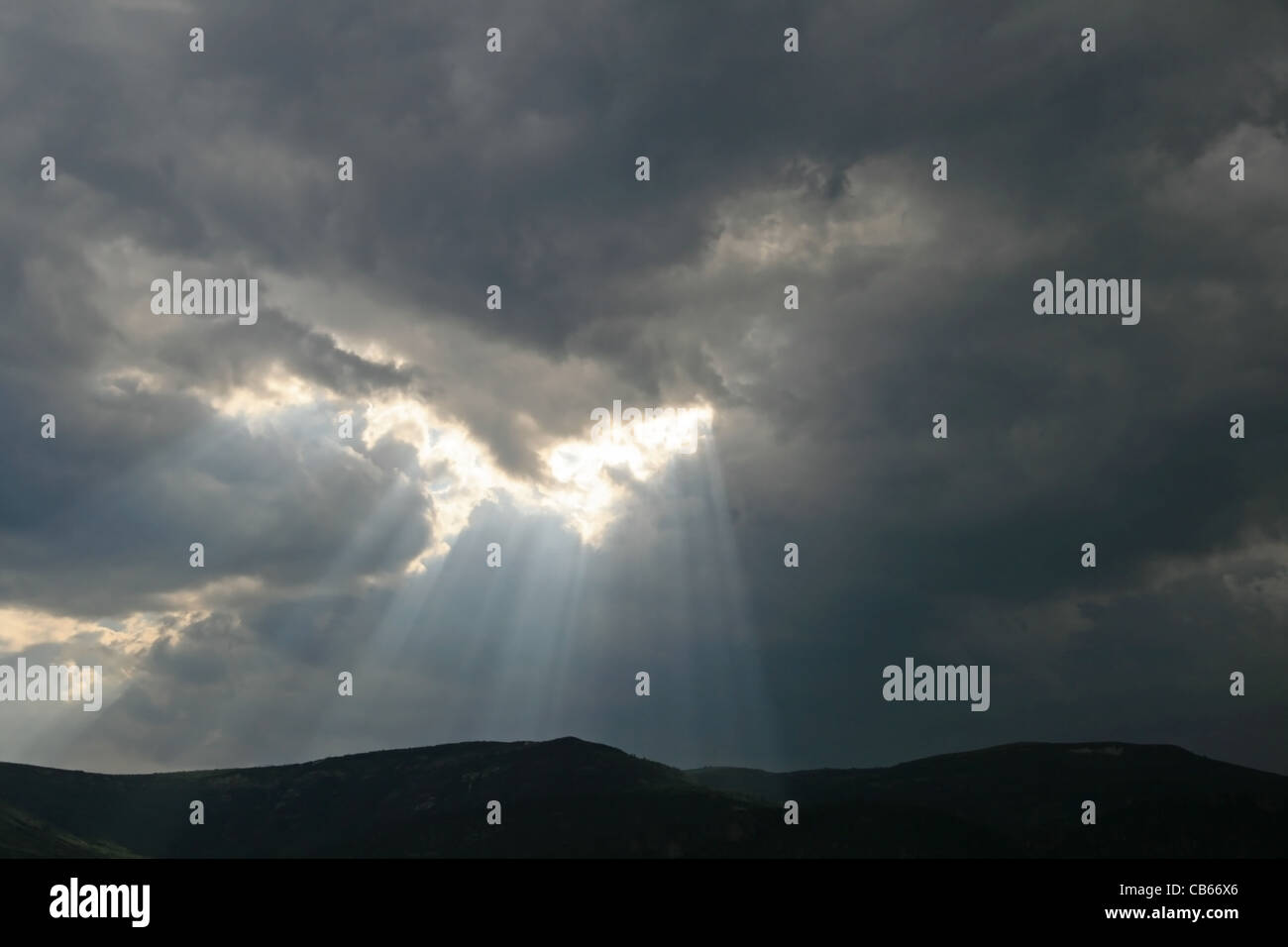 God rays emerge from dark cloudy sky over hills Stock Photo