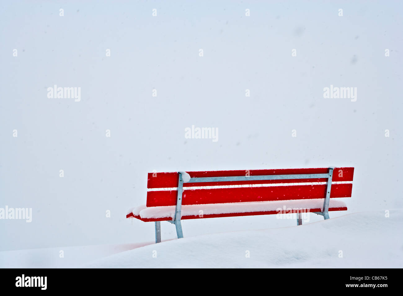Red bench surrounded by snow, still snowing, on a winter day. Stock Photo
