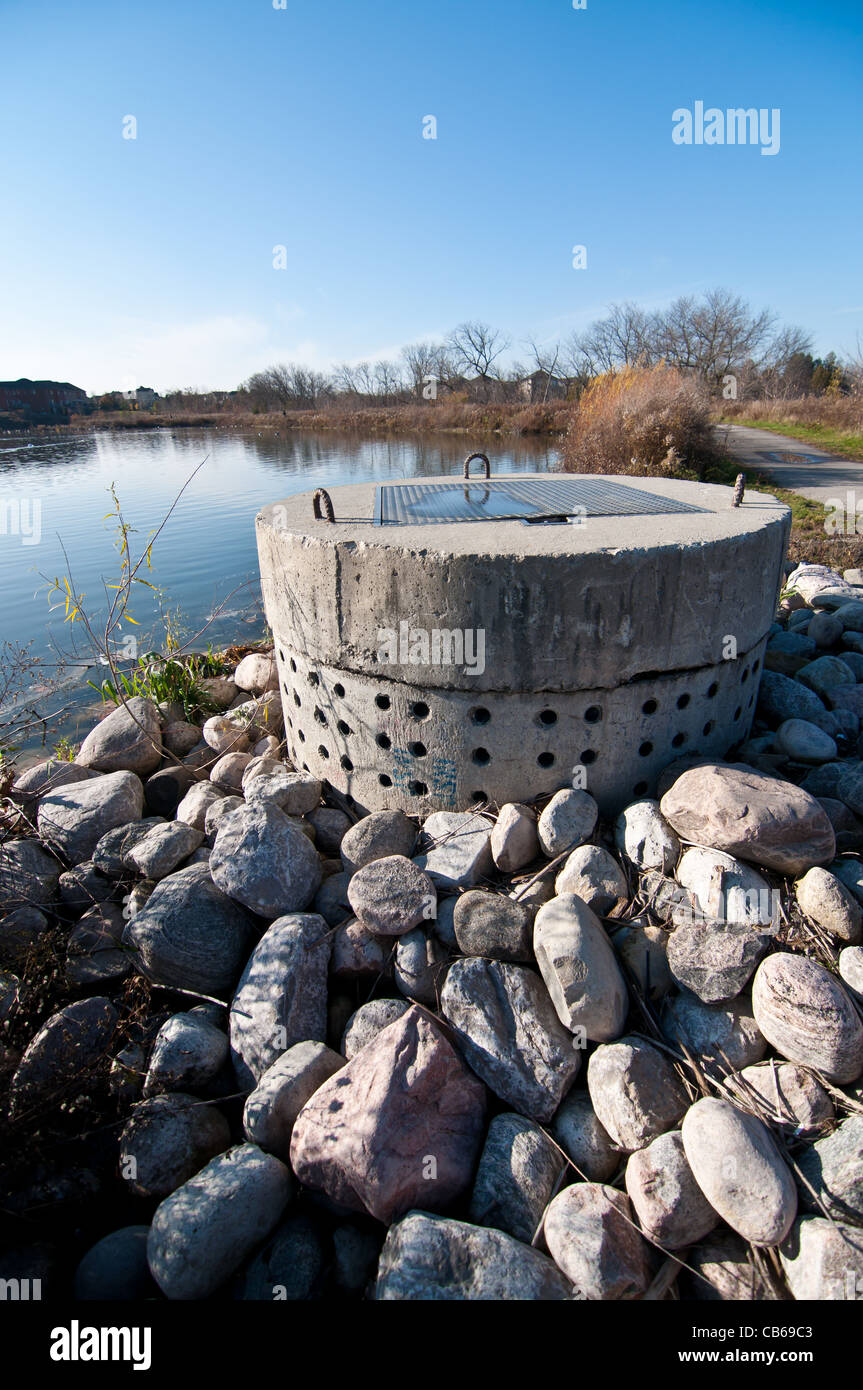 A perforated concrete pipe forms part of a stormwater management system in a suburban pond. Stock Photo