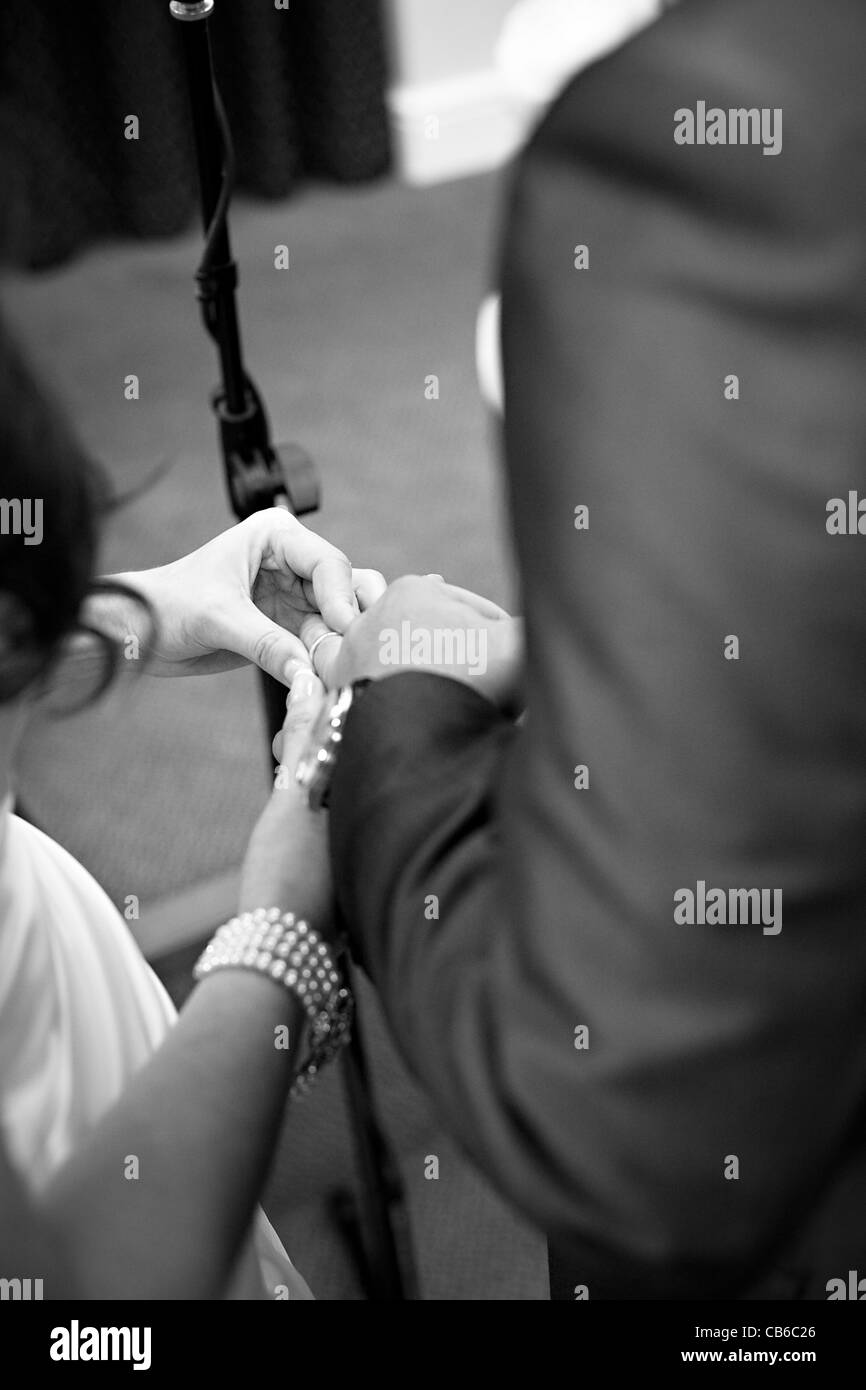 Black and white image of bride placing wedding ring on groom's ring finger during wedding ceremony. Stock Photo