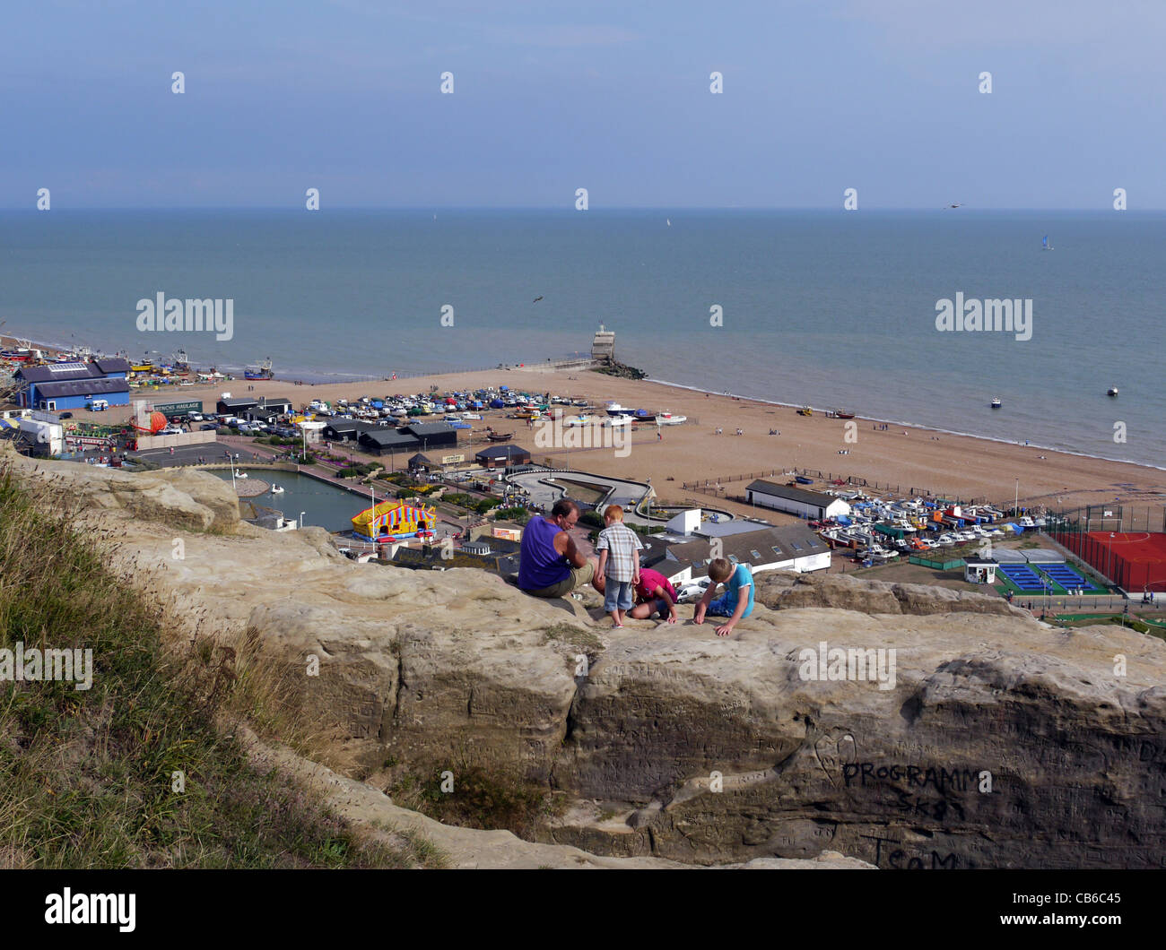 A view from the West Hill down towards Hastings seafront boating lake and lifeboat station with a family on the foreground rocks Stock Photo