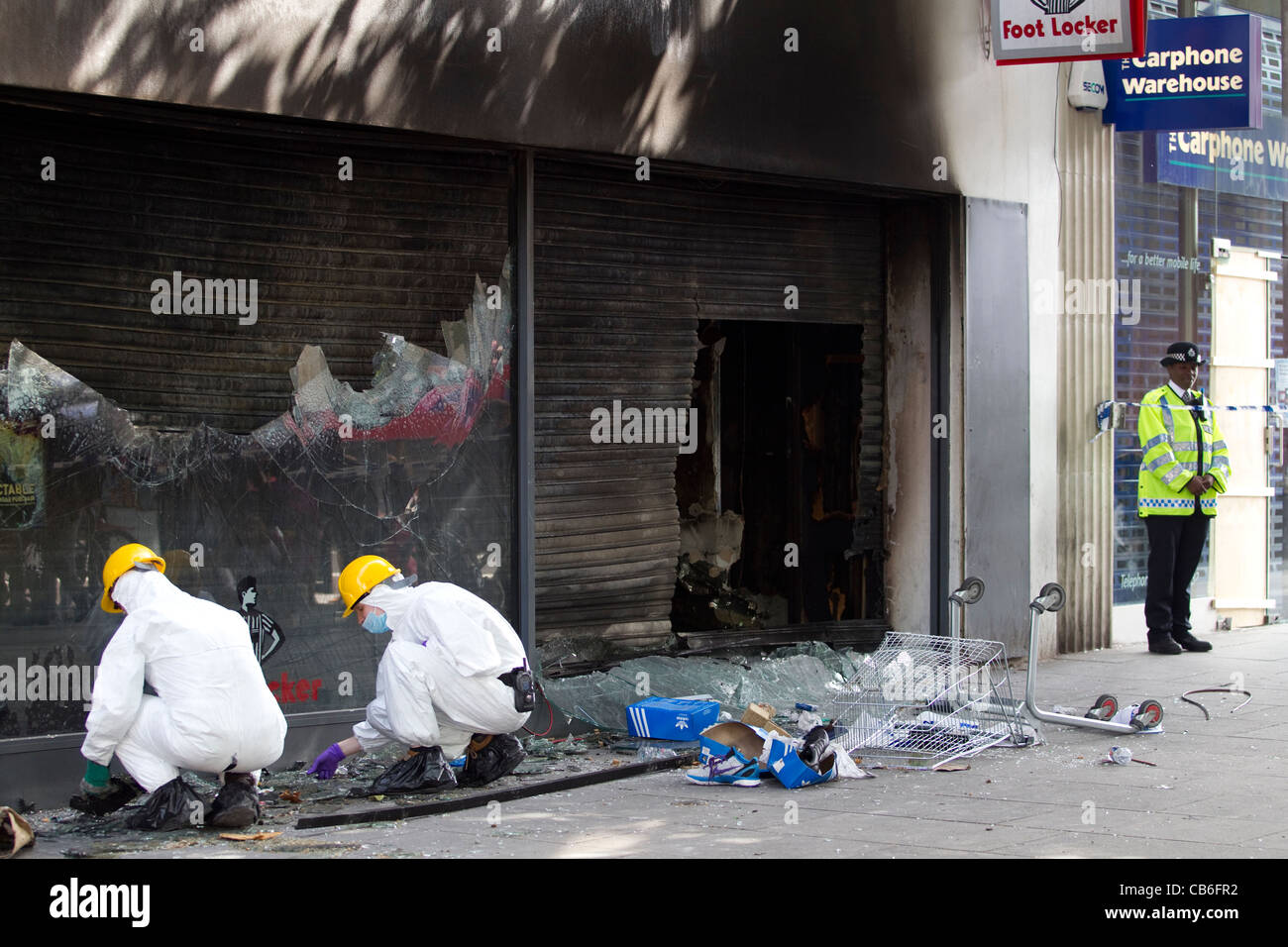 Police forensics search a burnt out Foot Locker sports wear store looted and set alight during rioting in Brixton, London. Stock Photo