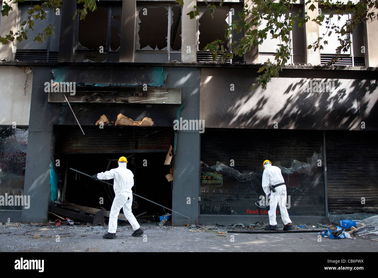 Police forensics search a burnt out Foot Locker sports wear store looted and set alight during rioting in Brixton, London. Stock Photo