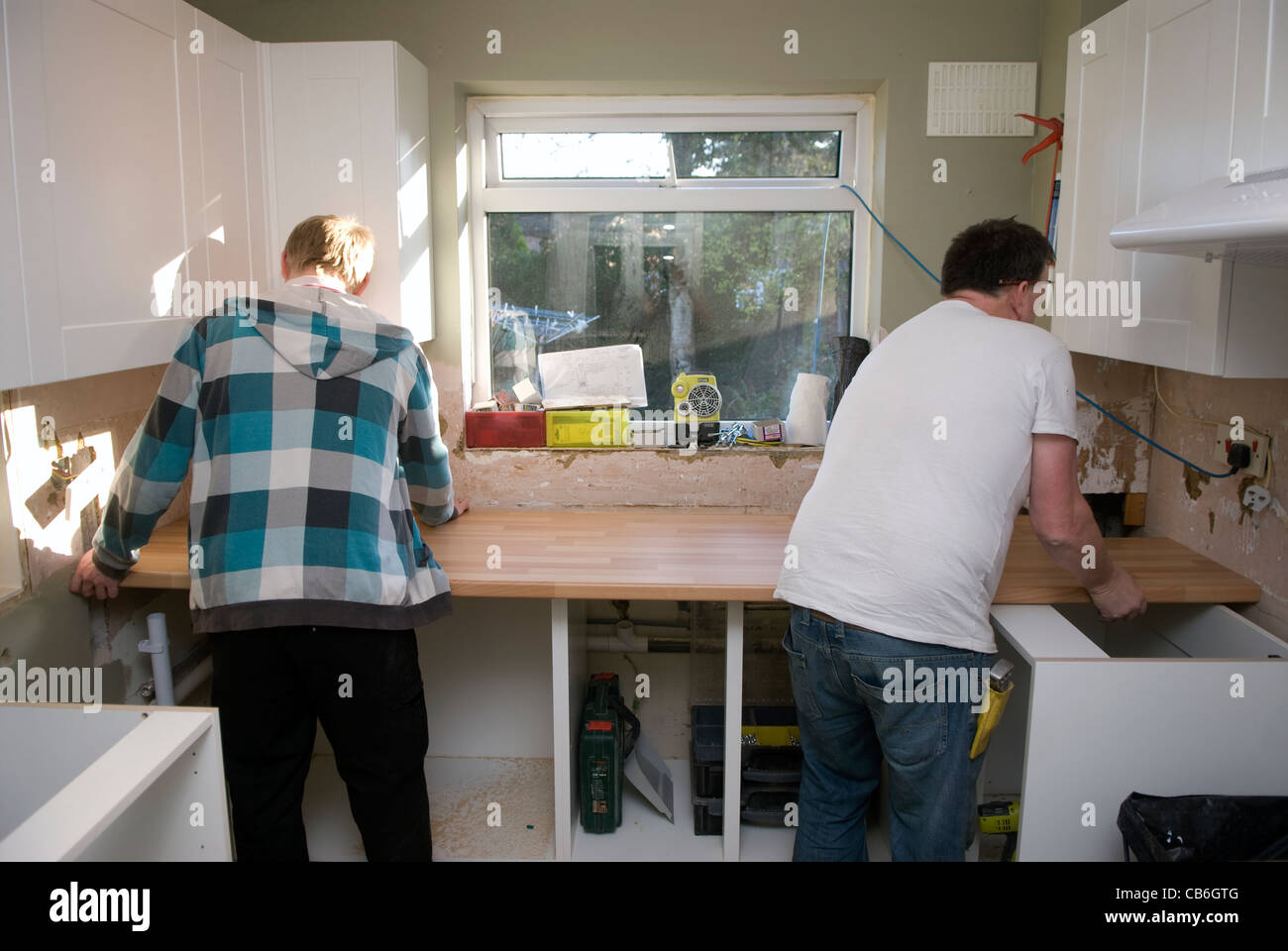 Tradesman (right) and his assistant positioning worktop in new kitchen installation in residential home, Bordon, Hampshire, UK. Stock Photo