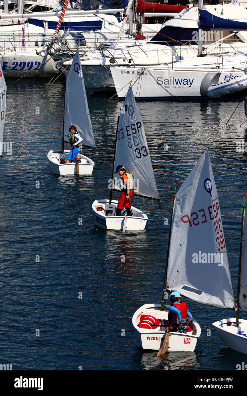 Schoolchildren setting off for sailing lessons in Optimist class sailing boats in marina, Vigo, Galicia, Spain Stock Photo