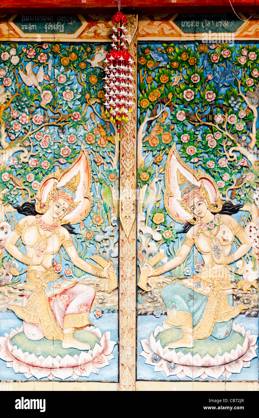 Elaborate Buddhist painted carving of female goddesses & flowers on shutter doors of old temple in northern Thailand Stock Photo
