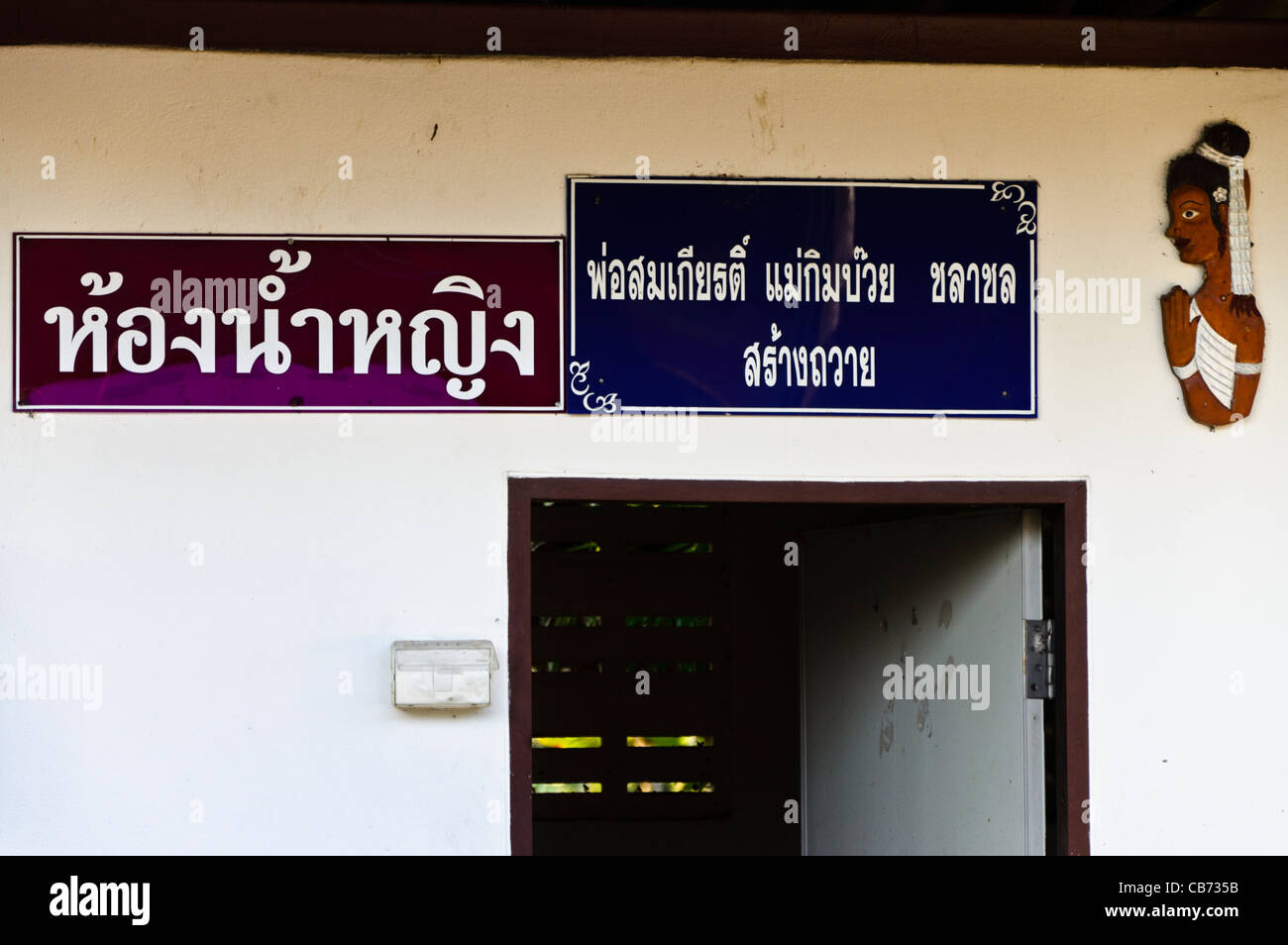 Closeup of restroom building with white walls & figure of a woman by door with Thai writing in northern Thailand Stock Photo