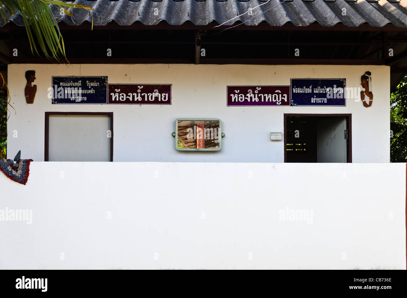 Restroom building with white walls & figures of man by left door and woman by right door with Thai writing in northern Thailand Stock Photo