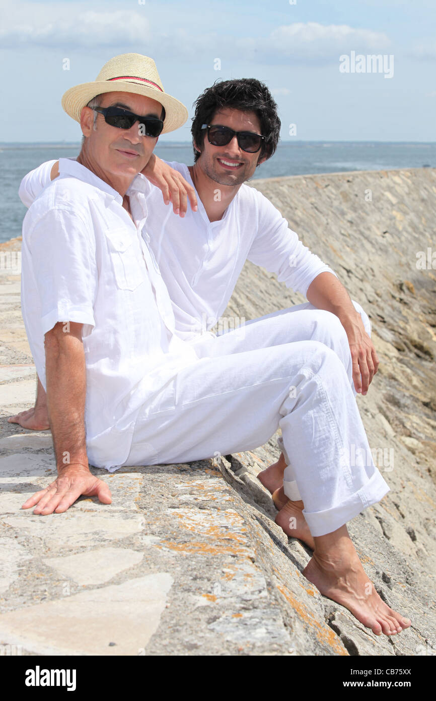 Grownup father and son sitting on a harbor wall Stock Photo