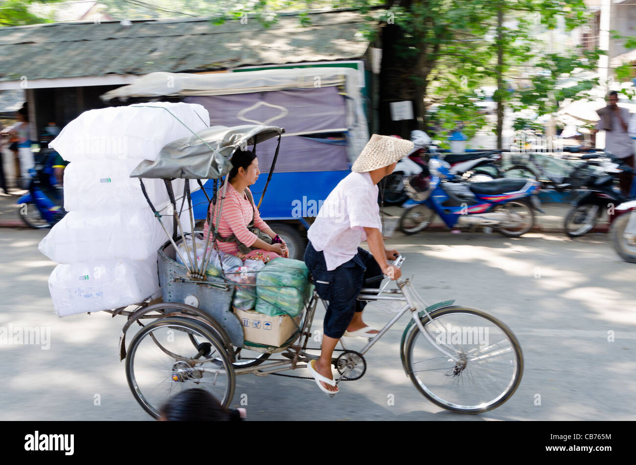 A man wearing a conical straw hat pedals a bicycle rickshaw with ...