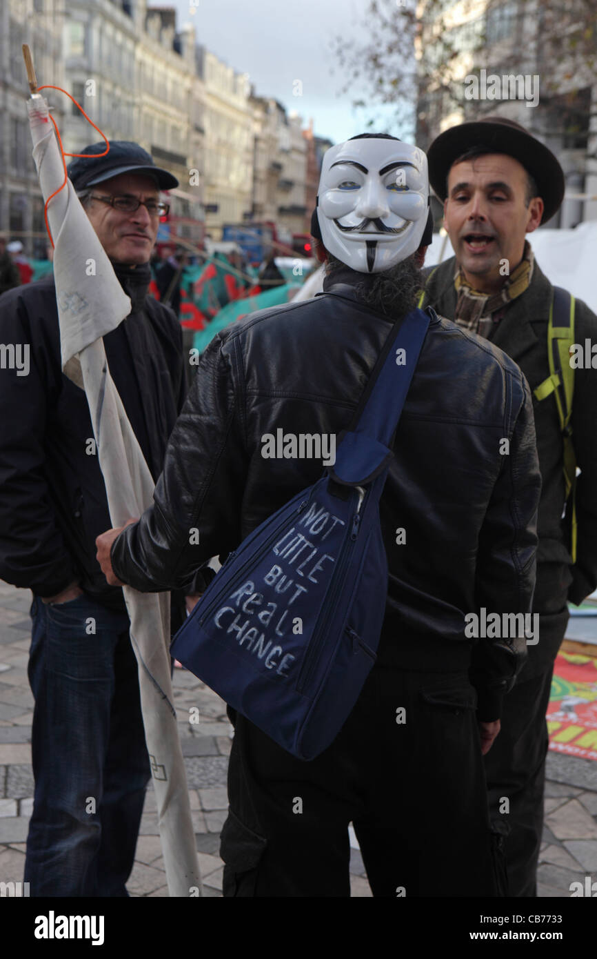two men talk to male member of Anonymous anarchist hackivist political protest group, Occupy London, St Paul's Cathedral. Stock Photo