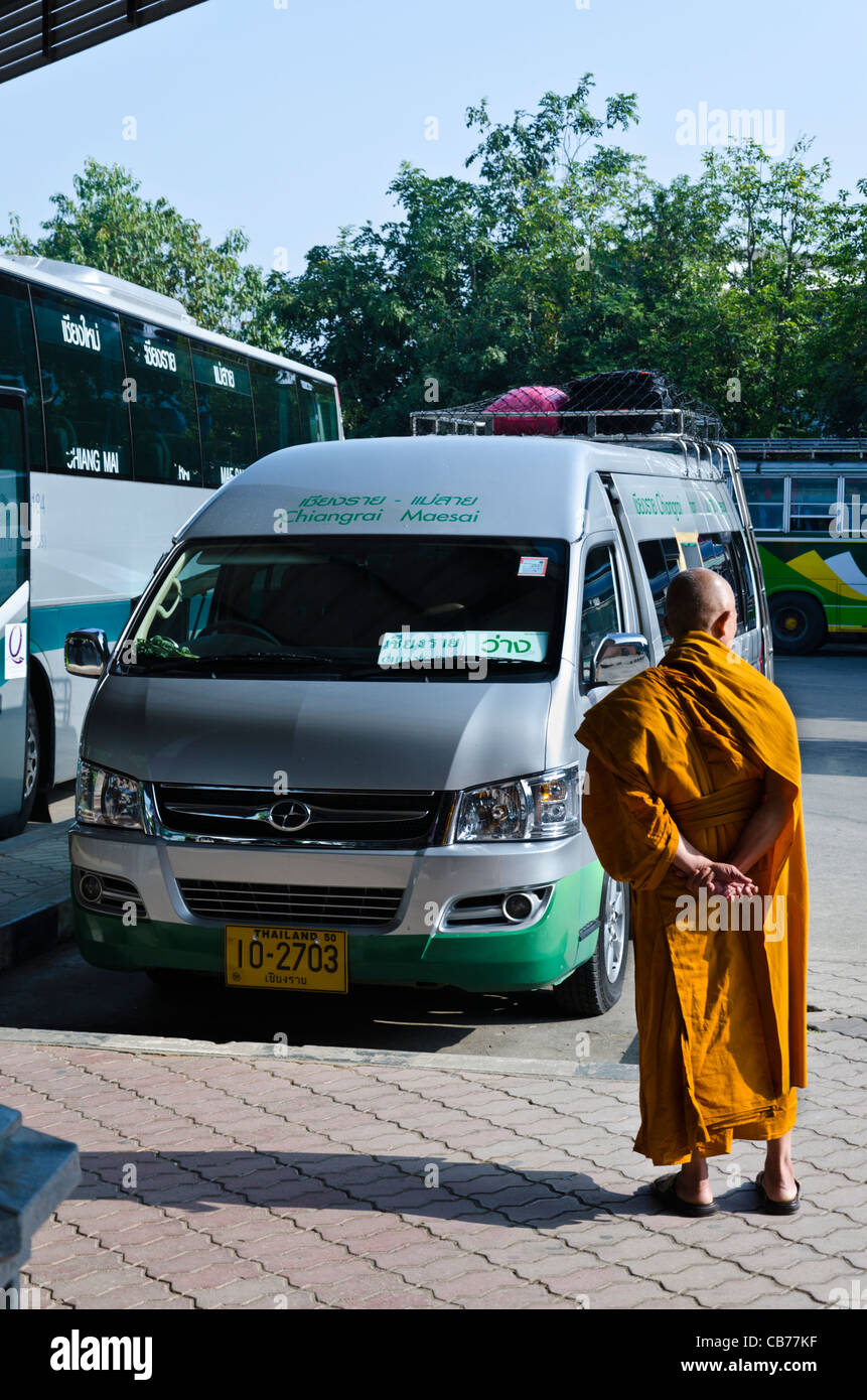 Buddhist monk in orange robe standing in sunshine next to silver van at bus station in Mae Sai in northern Thailand Stock Photo