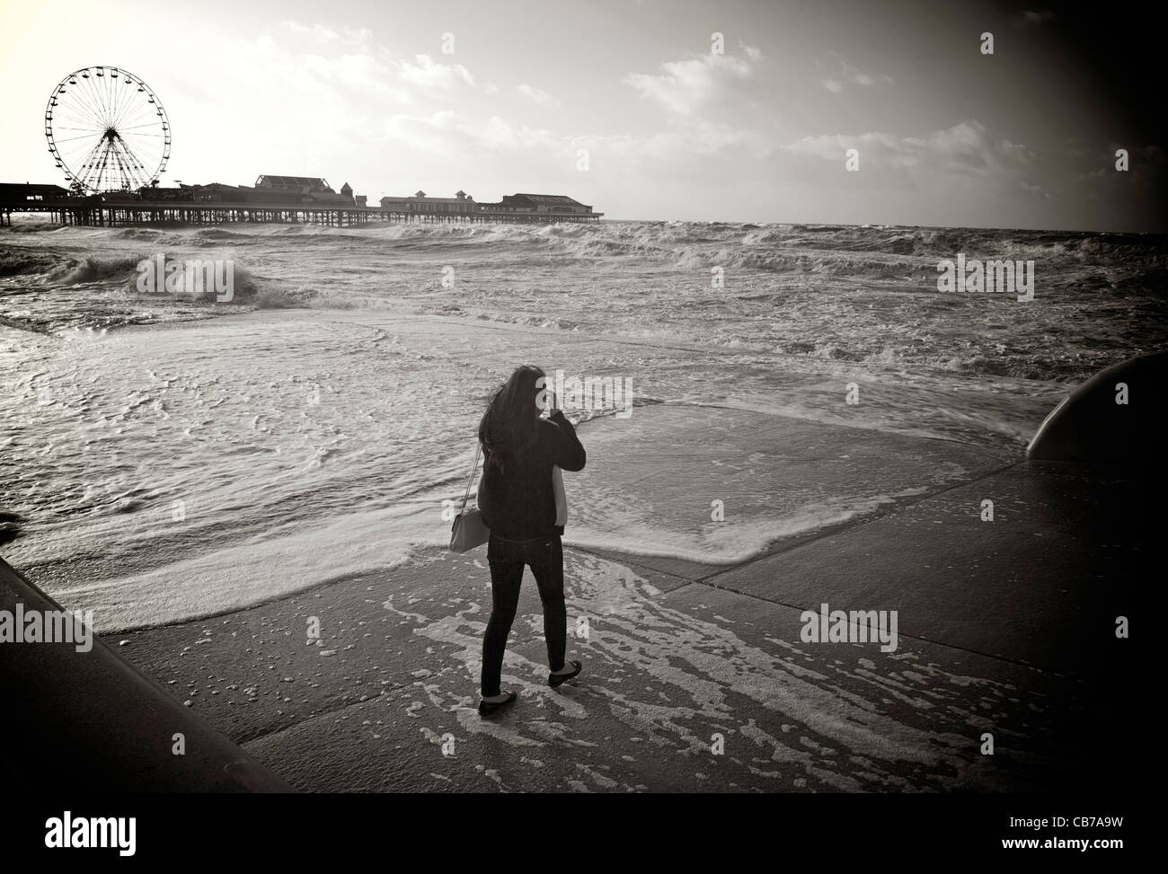 A young female tourist getting too close to  a stormy sea at high tide in Blackpool Stock Photo
