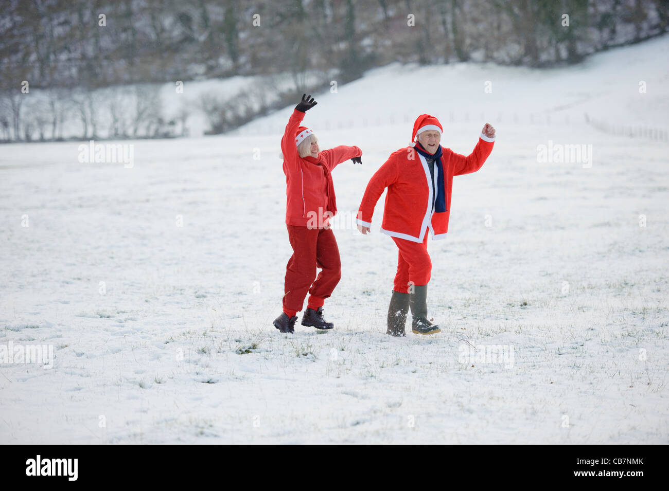 A happily retired couple play in the snow dressed as Father Christmas Stock Photo