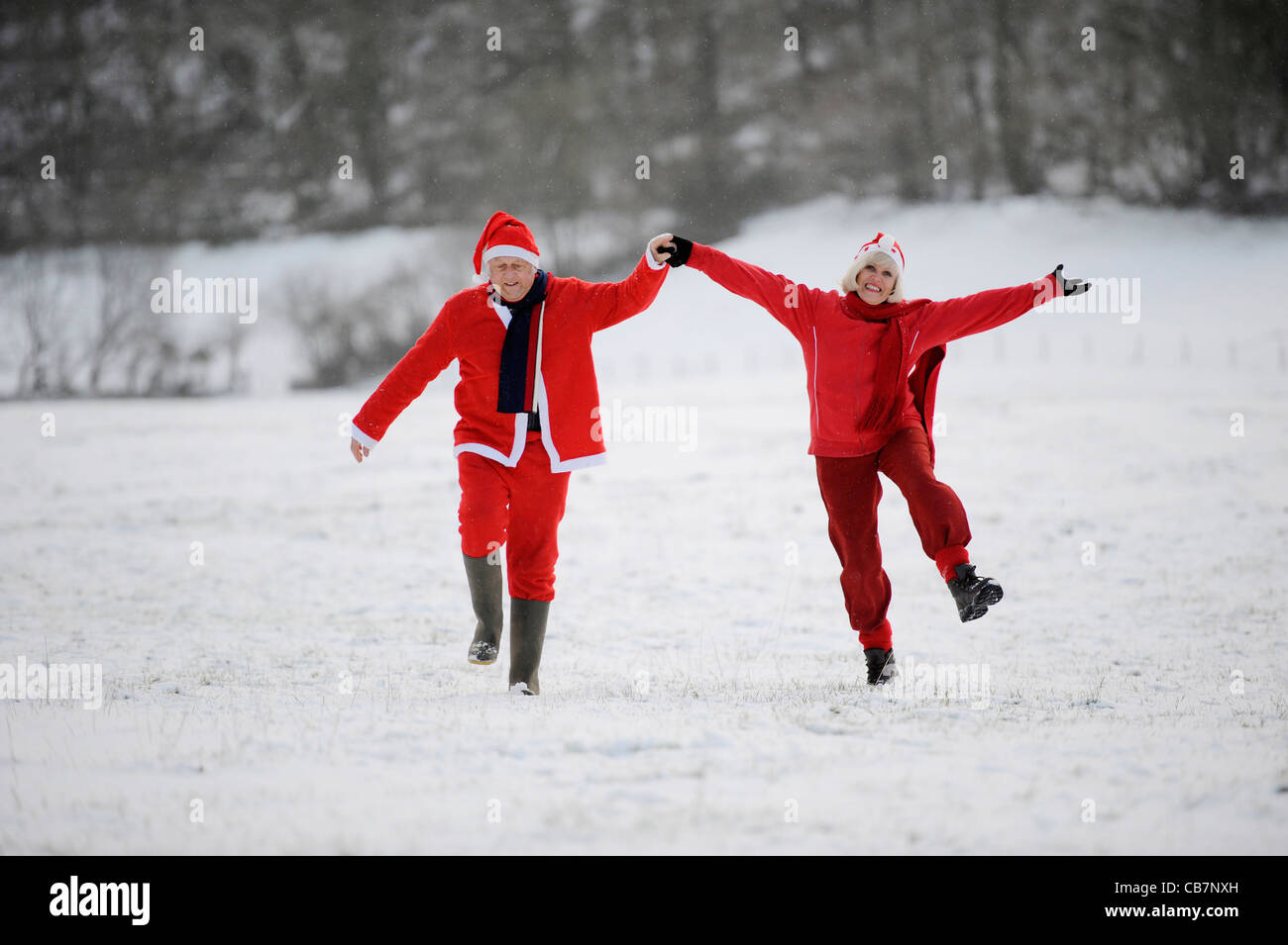 A happily retired couple play in the snow dressed as Father Christmas Stock Photo