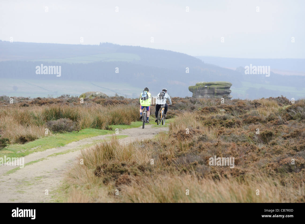 two cyclists riding across baslow edge derbyshire uk with the eagle stone in the background Stock Photo