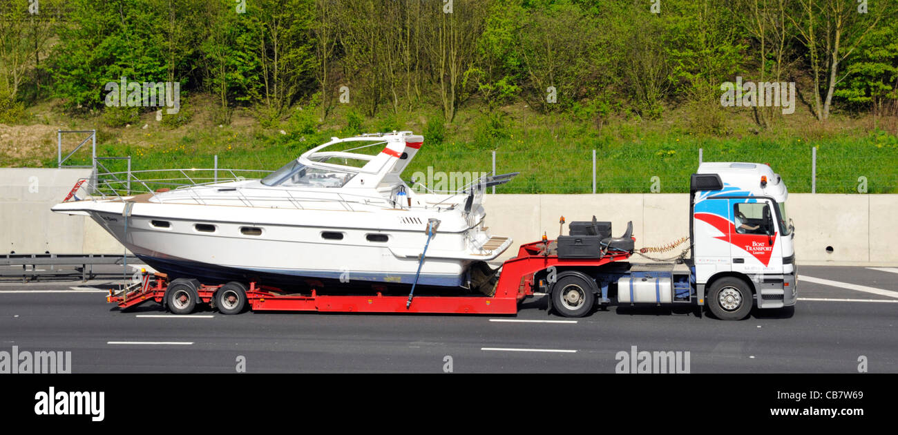 Specialist boat haulage contractor launch transporting on articulated low loader trailer & hgv lorry truck driving along M25 motorway Essex England UK Stock Photo