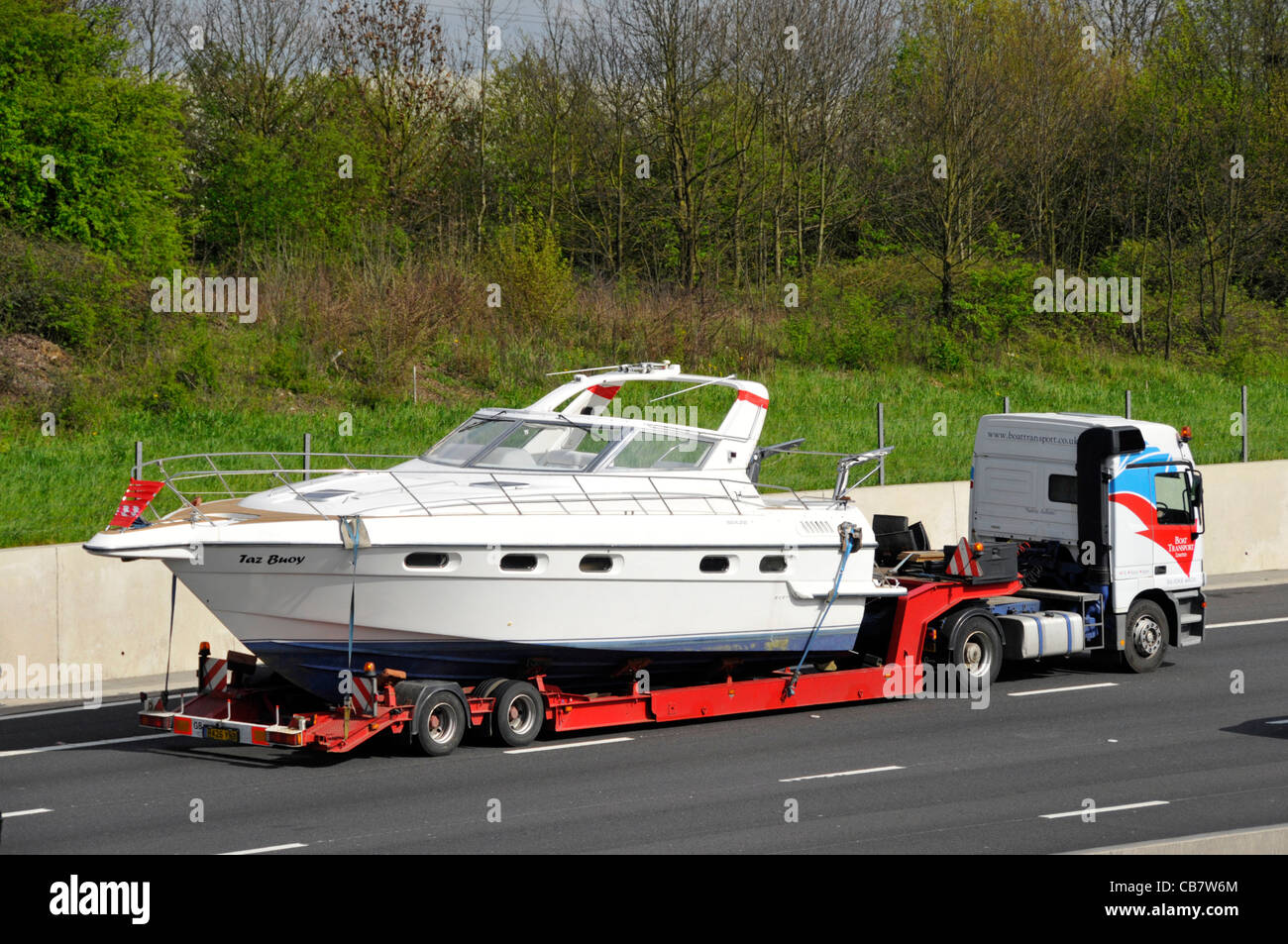 Specialist boat haulage contractor launch transportation on articulated low loader & hgv lorry truck driving along M25 motorway Essex England UK Stock Photo