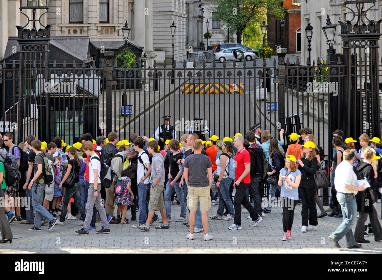 Armed London Metropolitan police officers behind security gate protect access to10 Downing Street tourists & group of school kids in caps Whitehall UK Stock Photo