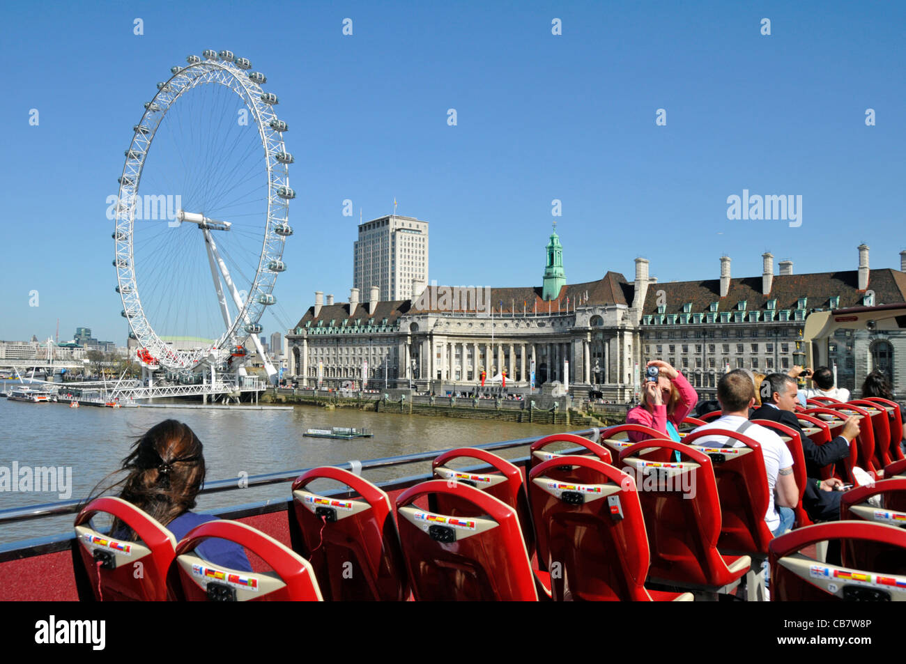Open top sightseeing tour bus blue sky sunny Spring day for tourists cross Westminster Bridge high tide views of River Thames & London Eye England UK Stock Photo