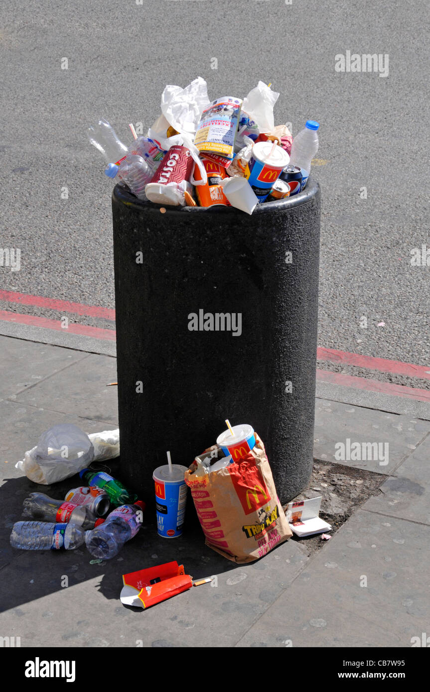 Waste management required to overflowing roadside litter bin full with rubbish garbage litter & trash spilling on pavement busy London street uk Stock Photo