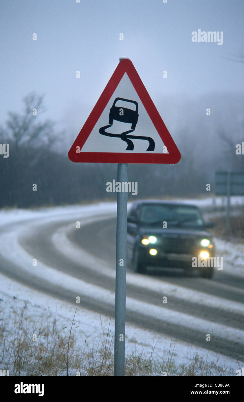 car travelling in winter snow passing warning sign of icy road near Leeds Yorkshire UK Stock Photo