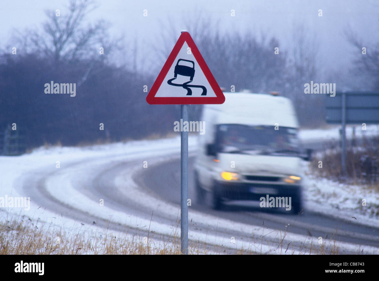 van travelling in winter snow passing warning sign of icy road near Leeds Yorkshire UK Stock Photo