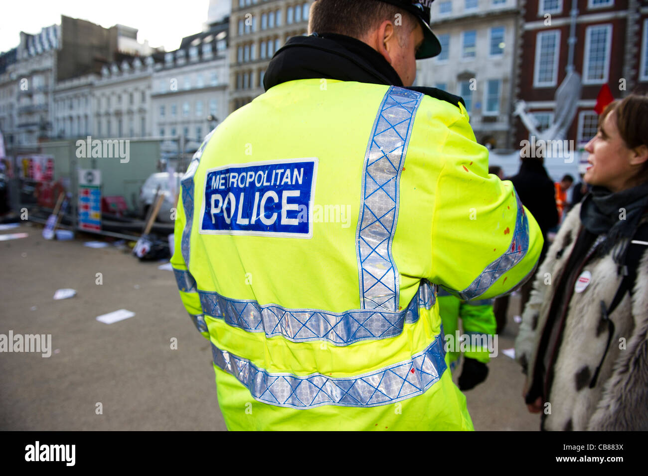 Rear view of Metropolitan police officer wearing high visibility jacket speaking to female member of the public. Stock Photo