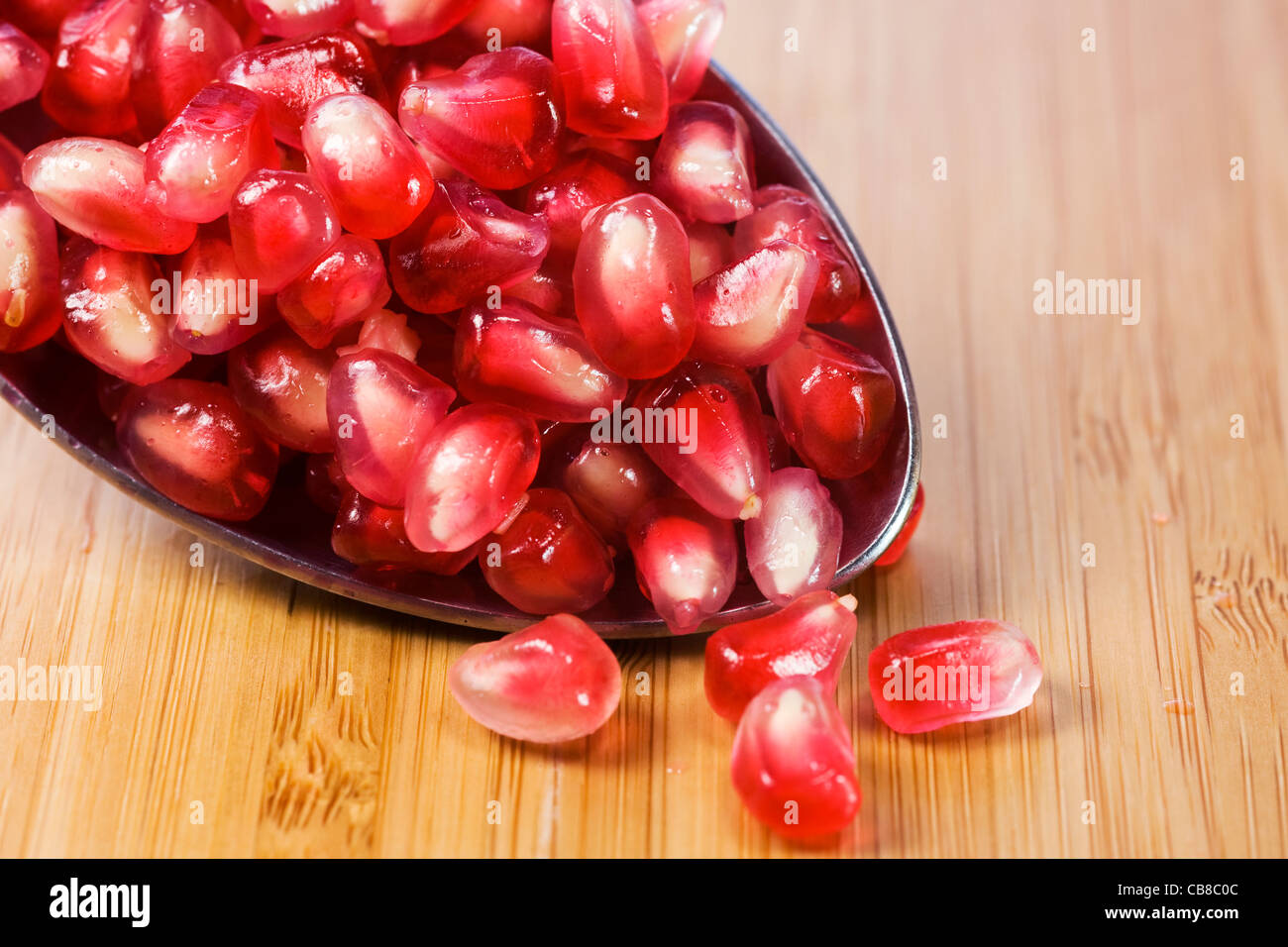 Punica granatum. A spoonful of pomegranate arils on a bamboo board. Stock Photo