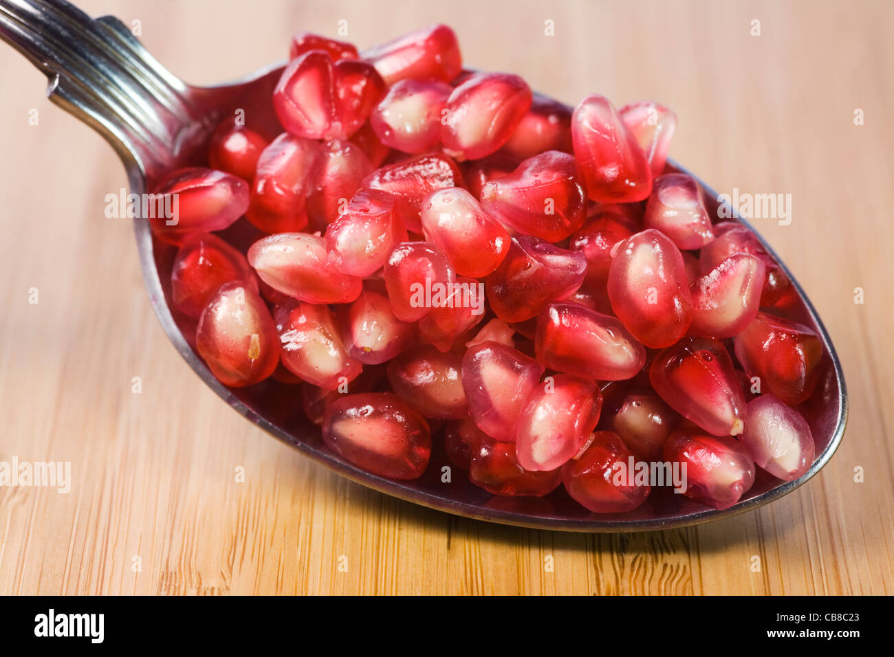 Punica granatum. A spoonful of pomegranate arils on a bamboo board. Stock Photo