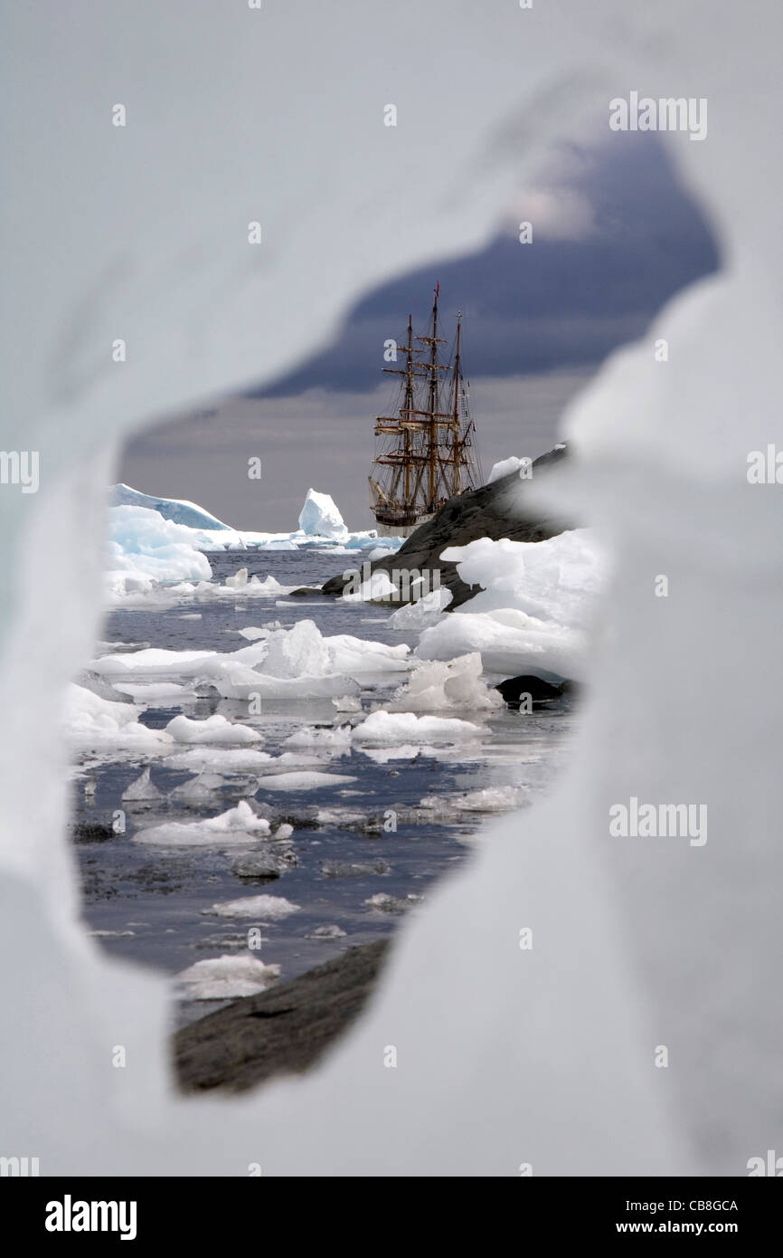 The tallship Europa, a three-masted barque seen through gap in iceberg in Antarctic sea at Port Charcot, Antarctica Stock Photo